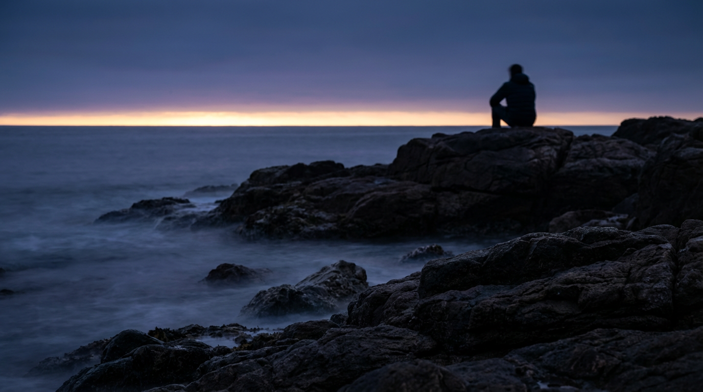 夜明け前の地平線に細い光の帯。人物は写らない。暗さの中にわずかな変化が見える静かな風景
