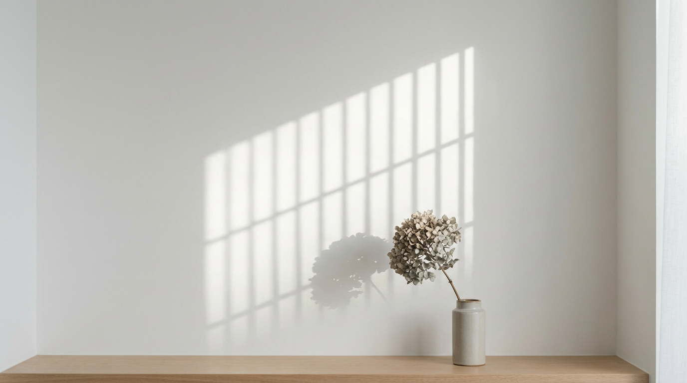 白い壁に映る窓格子の影と一輪の枯れ花、ミニマルな室内写真、人物は写らない